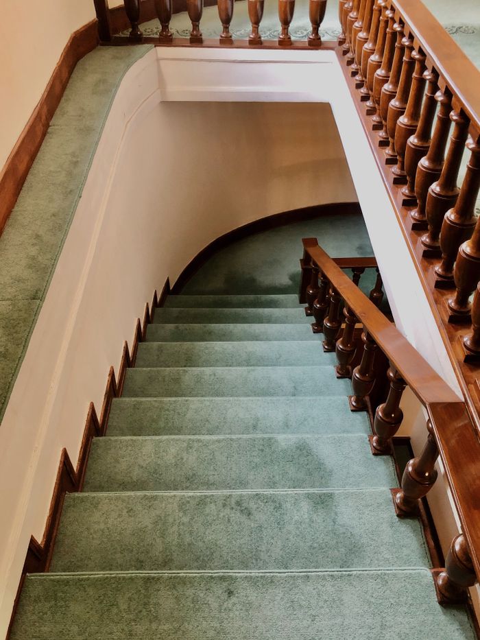 why-choose-us Top view of a classic carpeted staircase with wooden railing indoors.